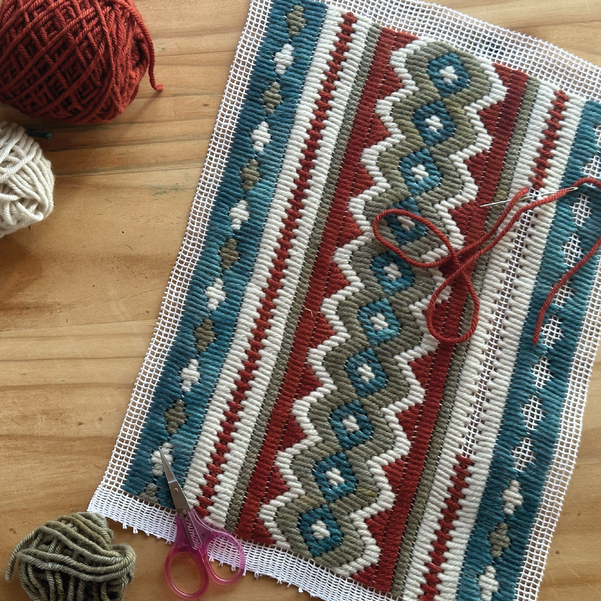Bargello sampler in progress on needlepoint canvas, with wools, needle and scissors